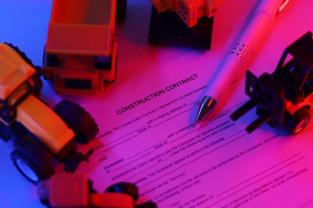 Construction contract with pen lies on table with many yellow construction and service toy vehicles